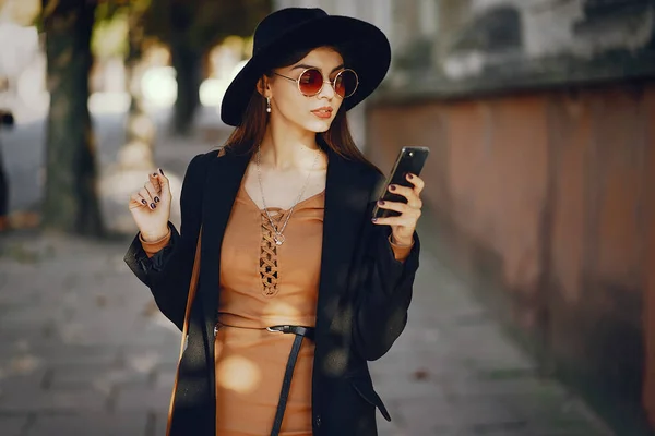 时尚女人在阳光灿烂的暖和天气里穿过城市时使用手机 — 图库照片