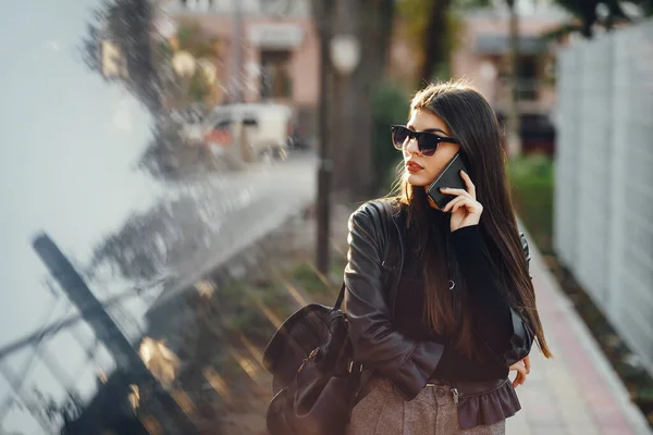 スタイリッシュな女性は晴れた暖かい日に街を歩くときに携帯電話を使います — ストック写真