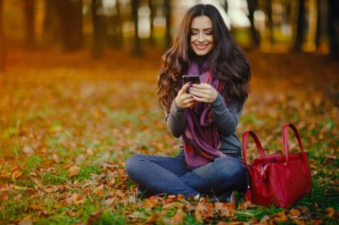 esmer kız parkta sonbahar sırasında rahatlatıcı olarak o telefonunu kullanarak