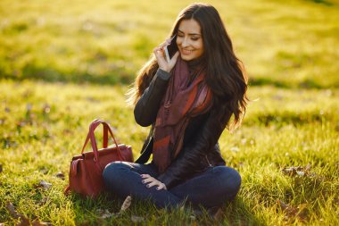 esmer kız parkta sonbahar sırasında rahatlatıcı olarak o telefonunu kullanarak