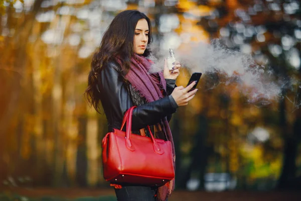Брюнетка Девушка Курит Электронную Сигарету Помощью Телефона Парке Drung Осень — стоковое фото
