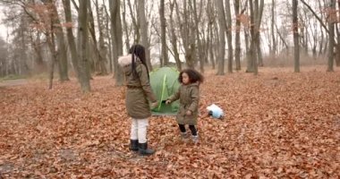 Ormanda sonbahar günü. Yaprakların üzerinde yürüyen ve çadırın yanında oynayan iki kız. Kamp, haftasonu, küçük kaşifler.