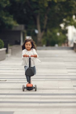 Parkta scooter kullanan bir çocuk. Çocuklar paten kaymayı öğreniyor. Küçük kız güneşli yaz gününde kayıyor.
