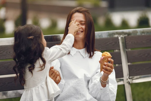 Family in a city. Little girl eats ice cream. Mother with daughter sitting on a bench.