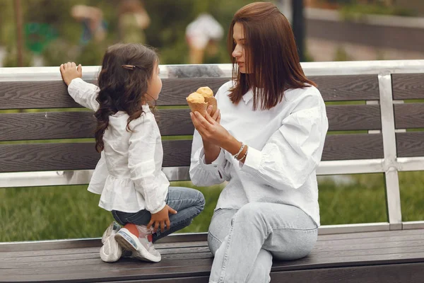 Family in a city. Little girl eats ice cream. Mother with daughter sitting on a bench.