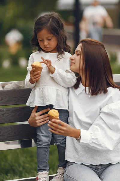 Family in a city. Little girl eats ice cream. Mother with daughter sitting on a bench.