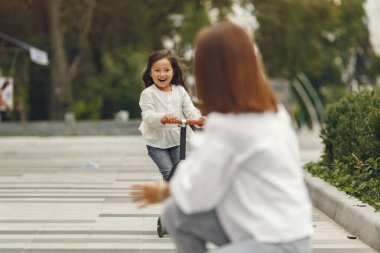 Mother and daughter on kick scooter in park. Kids learn to skate roller board. Little girl skating on sunny summer day.