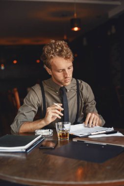 Adam viski içiyor. İşadamı belgeleri okur. Gömlek ve pantolon askılı yönetmen..