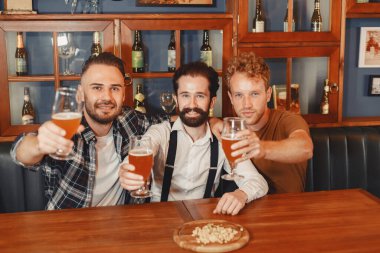 Arkadaşlarım ile toplantı. Casual üç mutlu genç erkeklerde konuşuyor ve otururken bar birlikte bira içme giymek.