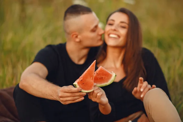 Couple in a field. Woman in a black blouse. Sunset background. People with watermelon.