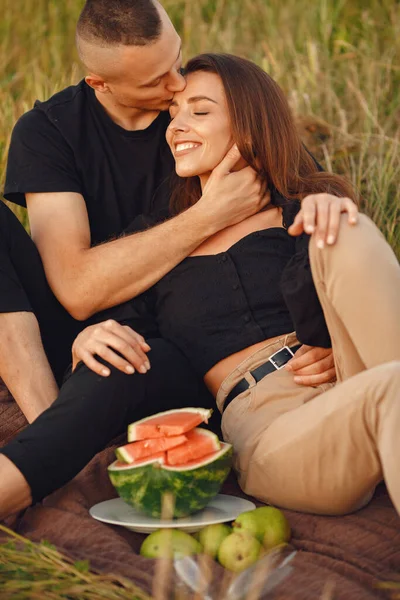 Couple in a field. Woman in a black blouse. Sunset background. People with watermelon.