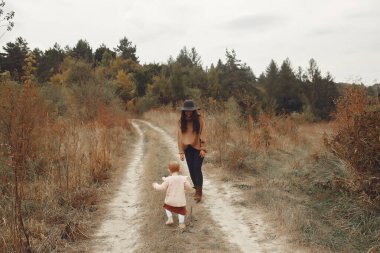 Sonbahar parkında bir aile. Kahverengi kazaklı anne. Sevimli küçük kız.