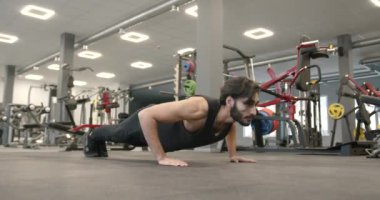 A young dark-haired athlete with a beard in a black sports uniform is squeezing off the floor in a modern gym. Maximum concentration on the exercise. Training concept
