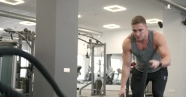 Athletic guy focuses on fitness training with ropes in the gym. Functional mens training.