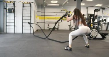 Athletic girl with long dark hair focused on fitness workout with ropes in the gym. Functional womens training