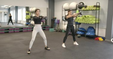 Two attractive dark-haired women perform fitness exercises with equipment. Functional womens training.
