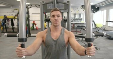 A young athlete in a gray T-shirt performs an exercise in a butterfly simulator. Strength training of pectoral muscles. Mens training