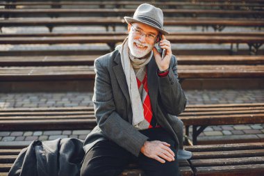 Yakışıklı dedesi bir sonbahar parkta. Yaşlı adam bir gri ceket ve şapka. Bankta oturan erkek