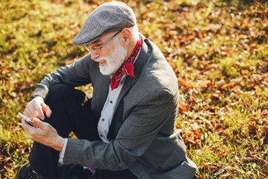 Yakışıklı dedesi bir sonbahar parkta. Yaşlı adam gri ceketli. Çimenlerin üzerinde oturan erkek