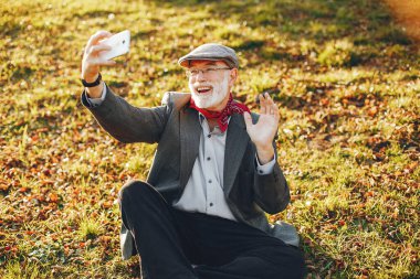 Yakışıklı dedesi bir sonbahar parkta. Yaşlı adam gri ceketli. Çimenlerin üzerinde oturan erkek