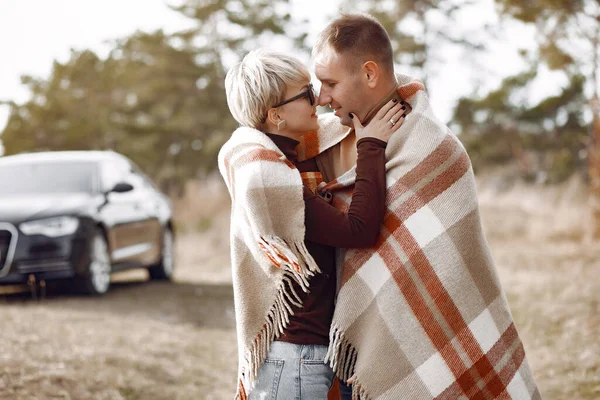 Couple in a field. Girl in a brown coat. Man with his wife near the car