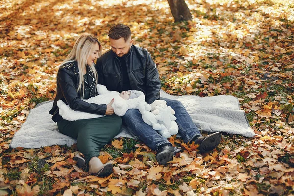 Family in a autumn park. Woman in a black jacket. Cute newborn little girl with parents