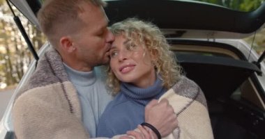 Close-up couple in love in jeans hiding in a blanket sitting in the trunk of a car. Autumn date in the park.