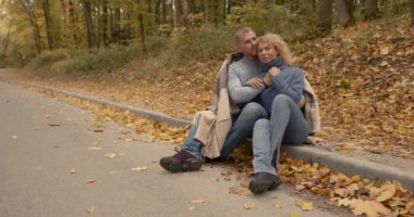 Young man and wife in jeans sitting on the sidewalk covered with a blanket.An open-air date