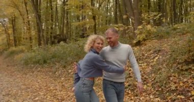 Young husband and wife in jeans walk along the alley in the park. Hold hands. Autumn date in the open air