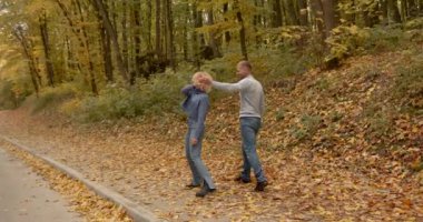 Young husband and wife in jeans walk along the alley in the park. Hold hands. Autumn date in the open air