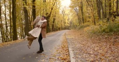 A young man holds his wife in his arms. Circling in the arms of the road. Autumn weekend outside the city