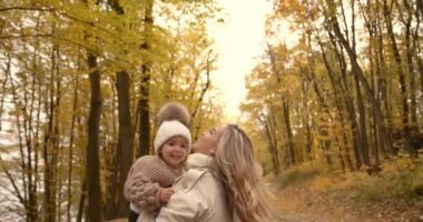 Young stylish mother holding a little baby in her arms. Circling in his arms with his daughter in the middle of the road in the park. Autumn family leisure