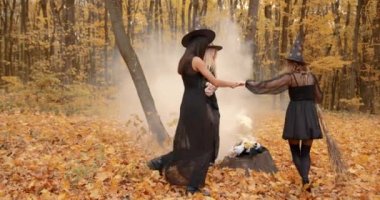 Halloween decorations. Autumn forest setting. Women dressed as wizzards dance in circle.