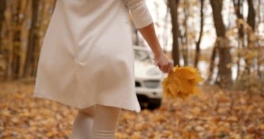 Woman going forward a white car. Lady in white clothing and bunch of yellow leaves.