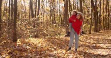 A young mother in a red jacket holds her daughter in her arms. Soak in the sun and smile. Happy family leisure