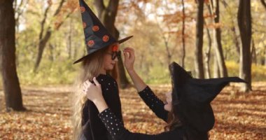 Beautiful brunette mom straightens her cute little daughters hair, they look like witches in special dresses and hats Halloween style