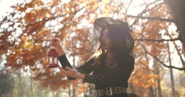 Beautiful brunette woman holding a street lamp in her hands. She looks like a witch in a special dress and chapel. Halloween style