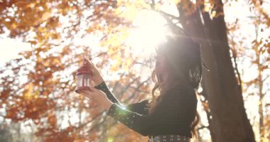 Beautiful brunette woman holding a street lamp in her hands. She looks like a witch in a special dress and chapel. Halloween style