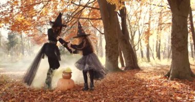 Beautiful brunette mom holding and cute little daughter circling over a jug. Yellow smoke spreads in clubs. They look like witches in special dresses and hats. Halloween style