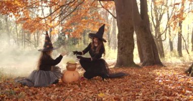 Beautiful brunette mom holding and cute little daughter circling over a jug. Yellow smoke spreads in clubs. They look like witches in special dresses and hats. Halloween style
