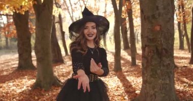 Attractive woman in a special dress and hat looks like a witch in the autumn forest. She poses. Halloween style