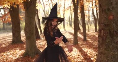 Attractive woman in a special dress and hat looks like a witch in the autumn forest. She poses. Halloween style