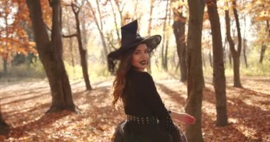 Attractive woman in a special dress and hat looks like a witch in the autumn forest. She poses. Halloween style