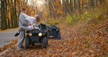 Young couple in opposite costumes on a date near ATVs. The guy hugs a girl sitting on an ATV. Active rest in the autumn forest.