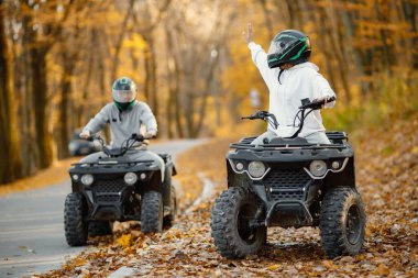 A young caucasian man and woman riding an ATV quad bikes in autumn forest. Two friends maneuvering off-road ATV. Couple wearing grey sportive costumes.