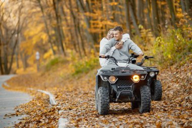 A young caucasian man and woman riding an ATV quad bike in autumn forest. Two friends maneuvering off-road ATV. Couple wearing grey sportive costumes.