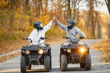 A young caucasian man and woman riding an ATV quad bikes in autumn forest. Couple holding hands. Couple wearing grey sportive costumes.