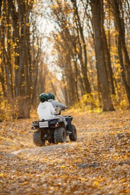 A young caucasian man and woman riding an ATV quad bike in autumn forest. Couple maneuvering off-road ATV. Couple wearing grey sportive costumes.