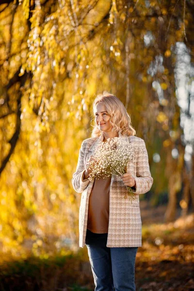 Portrait of middle-aged pregnant woman outdoors at park. Middle age pregnant woman expecting baby at aged pregnancy. Blonde woman wearing brown sweater and beige coat.