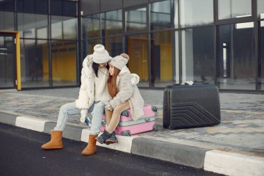 Brunette mother and her daughter going on vacation. Woman and girl sitting on a luggage and talking. Mother and daughter wearing warm clothes.